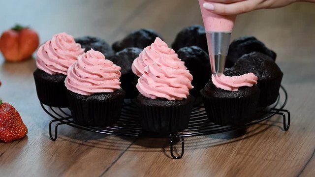 Woman decorating delicious homemade cupcakes with cream.
