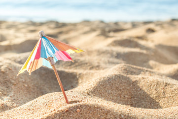 Decorative small paper umbrella in sand at sea beach.