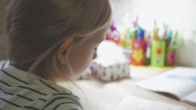 Cute girl making her homework, schoolgirl studing at home at the table, children's education.