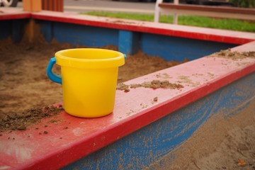 Yellow toy pail in the red sandbox. Sandbox toy
