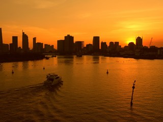 Silhouette of a boat speeding in the Mekong River with with sky scrapers and buildings in the background at sunset.