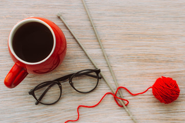 Large red cup with coffee, knitting needles, a ball of red yarn and glasses. Concept knitting at home.