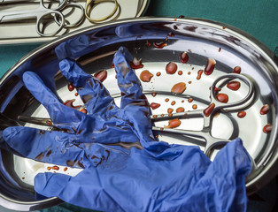 Gloves blue and scissors stained with blood on a tray in an operating theater, conceptual image