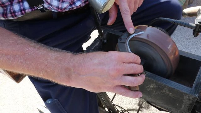hand of an old man grinds while sharpening his knife billhook blade on an old rotating millstone