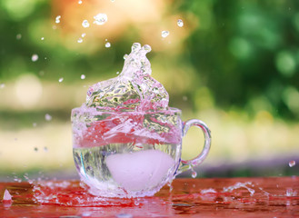 Splash of cool fresh water with ice cube in transparent glass cup in the table outoors in summer...