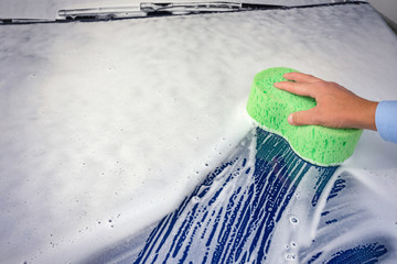 C man cleaning automobile with sponge at car wash. Ar wash with soap.