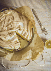 Flat lay view of delicious lemon meringue pie, one slice cut out on wooden table, vintage look.