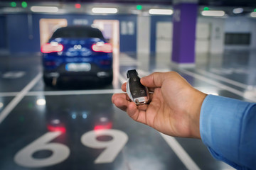 Car keys in a hand of the person against the background of the car. underground parking.