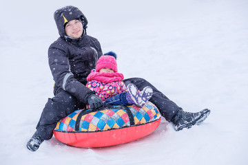 young father slides down from the snow hill on a tube with his little daughter