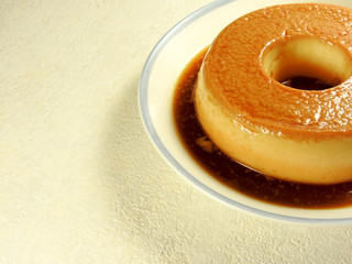 Close up of delicious handmade yellow color round egg pudding dessert with caramel sauce on blue side of the white plate isolated on white background.Sweet food.