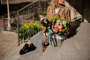 Woman in plaid coat sitting on concrete stairs with a wicker basket of flowers