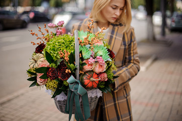 Blonde woman holding a lovely wicker basket of flowers against the city