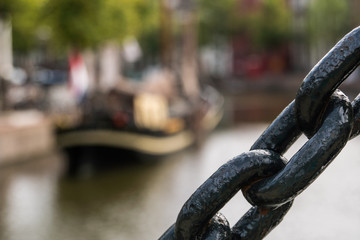 Black maritime Chain Close Up. Traditional wooden sailing ship with flag and sign on a board in channel blured on background. Old historic harbor of Schiedam, The Netherlands