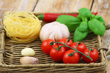 Ingredients for Italian pasta: spaghetti, tomatoes, garlic and fresh basil on wicker tray
