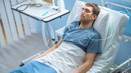 In the Hospital Sick Male Patient Sleeps on the Bed, He's Wearing Nasal Cannula to Help Him Breath....