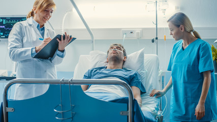 In the Hospital Male Patient Lies on the Bed, Professional Female Doctor Writes in the Patient Chart, Nurse Checks Drop Counter and Increases Dose of the Pain Killer.