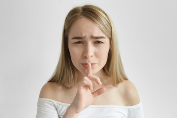 Naklejka premium Annoyed frustrated pretty girl whispering, making shush gesture while her children sleep. Beautiful stylish young female asking to speak more quietly, feeling tired, having frustrated expression