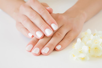Obraz na płótnie Canvas Young, perfect woman's hands with white nails. Care about nails and clean, soft, smooth skin. Manicure, pedicure beauty salon. Beautiful jasmine blossoms on table. Fresh flowers.