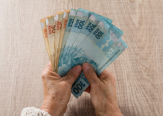 Brazilian currency: Real. Top view of old woman's hand handling bills.