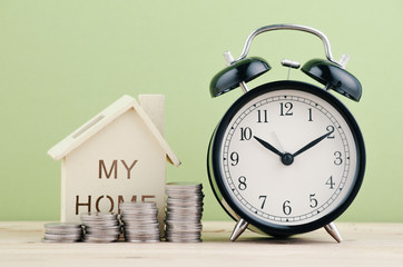 Taking time saving for dream house concept, stacking coins and alarm clock on wooden desk