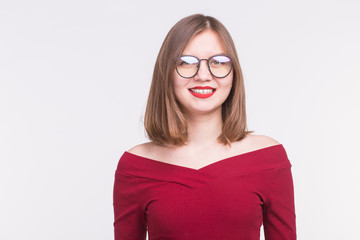 Fashion and people concept - Portrait of young smiling woman in glasses in red shirt on white background