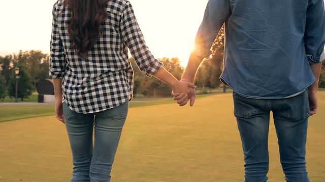 Close up footage of couple holding hands and walking outdoors. Sunset time. View from back.
