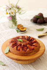 Sweet cake with caramelized plums, plums and a bouquet of flowers on the table. Rustic style.