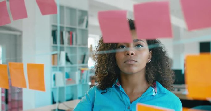 African American black employee looking onto a glass wall with sticky notes, framework for managing work, scrum methodology. 4K UHD 60 FPS SLOW MOTION