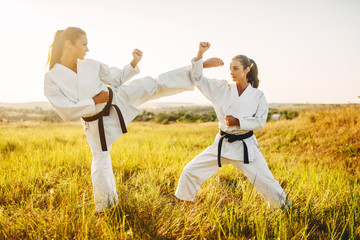 Fototapeta na wymiar Two female karate with black belts fight in field