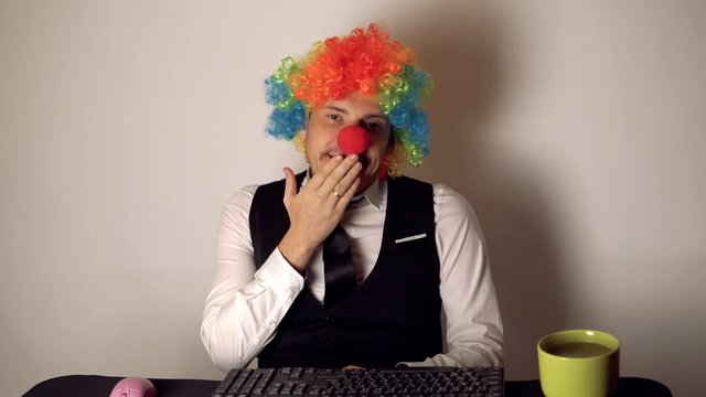 Office worker in the form of a clown working in the office at the computer. The concept of a clown at work, slacker