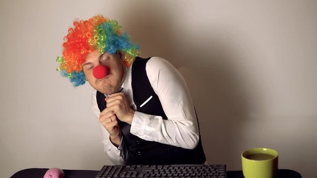 Office worker in the form of a clown working in the office at the computer. The concept of a clown at work, slacker