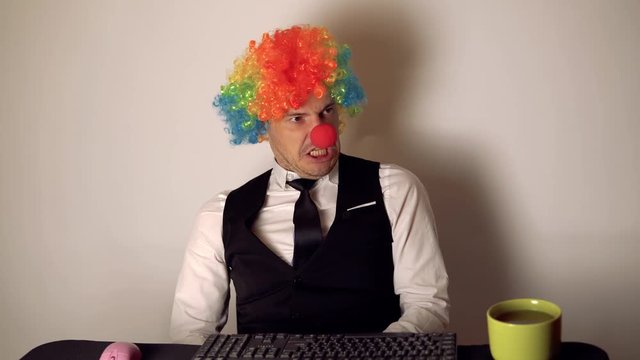 Office worker in the form of a clown working in the office at the computer. The concept of a clown at work, slacker