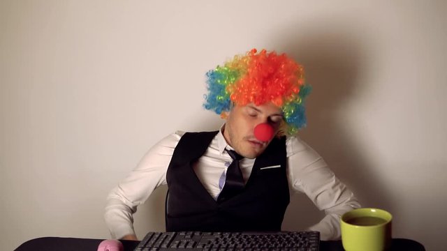 Office worker in the form of a clown working in the office at the computer. The concept of a clown at work, slacker