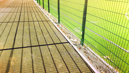 Fototapeta na wymiar road near lawn field for playing minifootball behind the green fence mesh