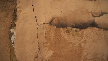 cracks in an old brown plastered and painted wall