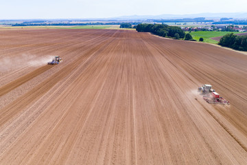 Tractors harrownig the large brown field