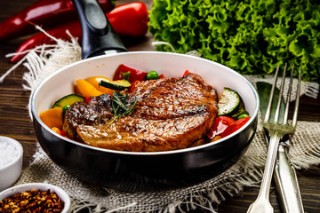 Grilled steak with vegetables in pan on wooden table