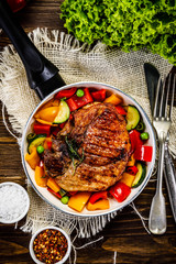 Grilled steak with vegetables in pan on wooden table