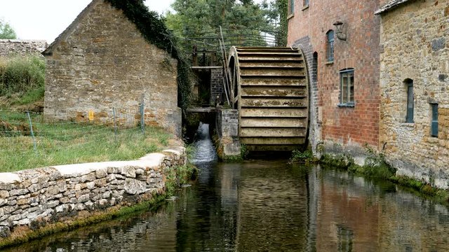Water from River Eye running through the village of Lower Slaughter flows past The Old Mill Water Wheel a 19th century water mill with an undershot wheel