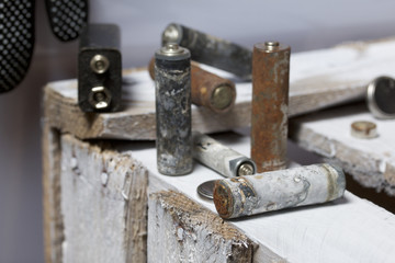 Used finger-wound batteries covered with corrosion. They lie on a wooden box. Next working gloves. Recycling.
