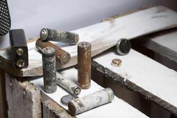 Used finger-wound batteries covered with corrosion. They lie on a wooden box. Next working gloves. Recycling.