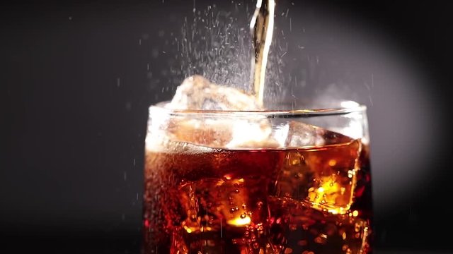Cola with Ice and bubbles in glass slow motion.
