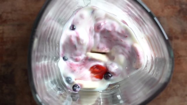 Smoothie blended in slow motion shot from above using fruit strawberries, bananas and yoghurt. Fruit mixing into blender, top view. Healthy eating, food, dieting and vegetarian concept