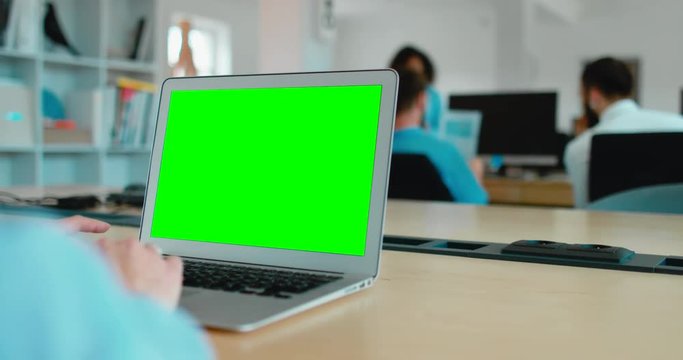 Young Caucasian woman sitting in the office, working on a laptop, green screen chroma key. 4K UHD 60 FPS SLO MO