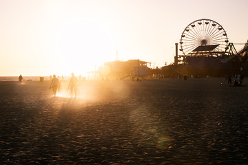 Silhouettes of people walking along Santa Monica beach and amusement park at sunset, Los Angeles, California
