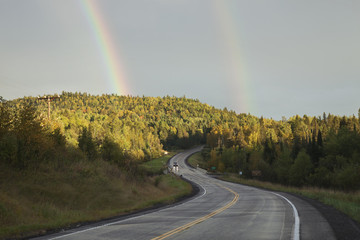 Double rainbow above road curving through hills in northern Minnesota during autumn