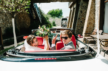 Happy bride and groom, newlywed wedding couple is driving a convertible retro car with balloons on...