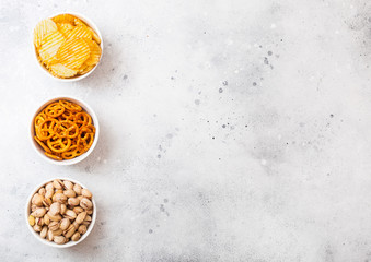 Pretzel and potato crisps and pistachio in white ceramic bowl on stone kitchen table background. Space for text. Snack for beer