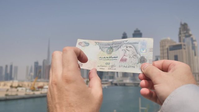A man holds a banknote in the hands of 500 dirhams against the background of the city of Dubai. Money United Arab Emirates.