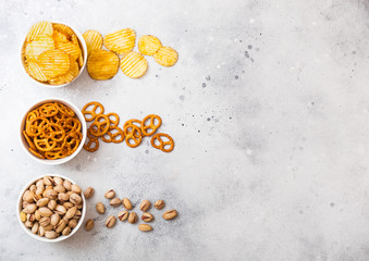 Pretzel and potato crisps and pistachio in white ceramic bowl on stone kitchen table background. Space for text. Snack for beer